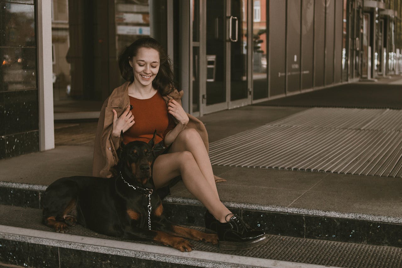 Happy woman sitting on steps with a Dobermann dog. Urban outdoor scene.